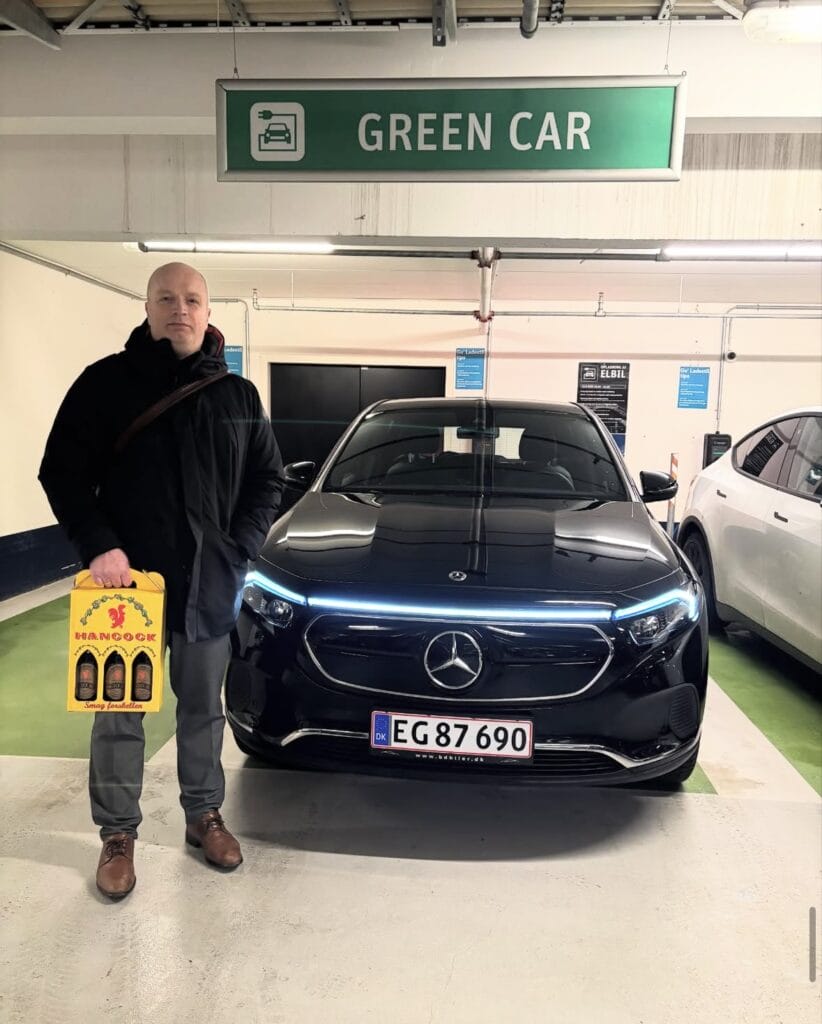 Mand ved sort elbil i grøn bil parkering